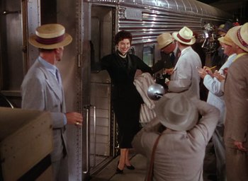 Movie still from “The Band Wagon” (1953), directed by Vincente Minnelli – A group of people standing next to each other near a train; Wide shot, High angle