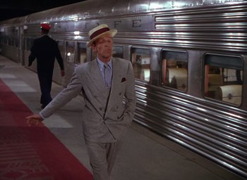 Movie still from “The Band Wagon” (1953), directed by Vincente Minnelli – A man in a suit and a hat walking by a train; Wide shot, Over the shoulder angle
