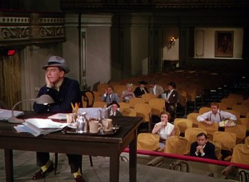 Movie still from “The Band Wagon” (1953), directed by Vincente Minnelli – A man sitting at a table in front of a group of people; Wide shot, High angle