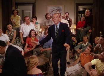 Movie still from “The Band Wagon” (1953), directed by Vincente Minnelli – A man in a suit and tie standing in front of a group of people; Wide shot, High angle