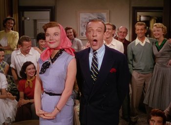 Movie still from “The Band Wagon” (1953), directed by Vincente Minnelli – A man and a woman standing next to each other in front of a group of people; Medium shot, Low angle