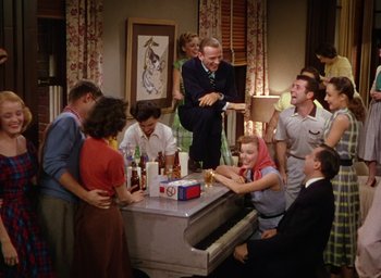 Movie still from “The Band Wagon” (1953), directed by Vincente Minnelli – A group of people standing around a piano; Wide shot, High angle