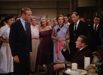 Movie still from “The Band Wagon” (1953), directed by Vincente Minnelli – A group of people standing in a room with candles; Medium shot, Over the shoulder angle