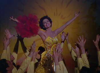 Movie still from “The Band Wagon” (1953), directed by Vincente Minnelli – A woman in a yellow dress is surrounded by a crowd; Medium shot, Low angle