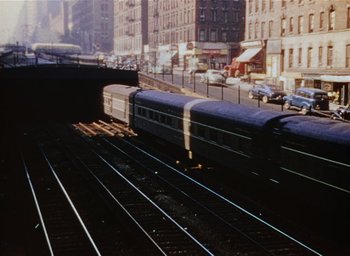 Movie still from “The Band Wagon” (1953), directed by Vincente Minnelli – A train traveling down train tracks next to buildings; Extreme Wide shot, High angle