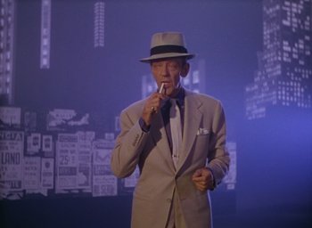 Movie still from “The Band Wagon” (1953), directed by Vincente Minnelli – An older man in a suit and hat is holding a microphone; Medium shot, Low angle