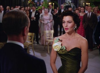 Movie still from “The Band Wagon” (1953), directed by Vincente Minnelli – A woman in a green dress standing in front of a crowd of people; Medium shot, Over the shoulder angle