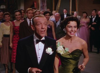 Movie still from “The Band Wagon” (1953), directed by Vincente Minnelli – A man and a woman in formal wear standing next to each other in front of a crowd; Medium shot, Low angle
