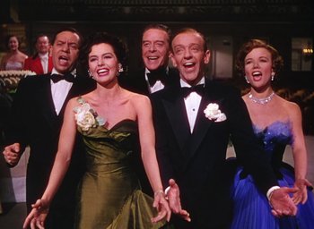 Movie still from “The Band Wagon” (1953), directed by Vincente Minnelli – A group of men and women in tuxedos holding hands; Medium shot, Low angle