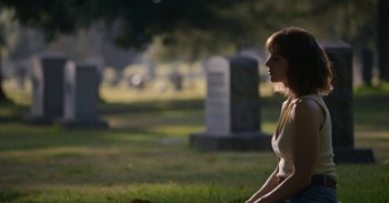 Movie still from “Horse Girl” (2020), directed by Jeff Baena – A woman sitting in the grass in front of a cemetery; Medium shot, Over the shoulder angle