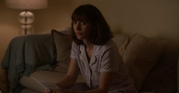 Movie still from “Horse Girl” (2020), directed by Jeff Baena – A woman sitting on a couch in a living room; Medium shot, Over the shoulder angle
