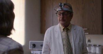 Movie still from “Horse Girl” (2020), directed by Jeff Baena – An older man wearing a white lab coat and a hat; Close Up shot, Over the shoulder angle