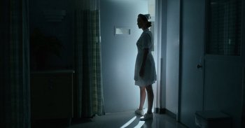 Movie still from “Horse Girl” (2020), directed by Jeff Baena – A woman standing in a hospital room looking out a window; Wide shot, Low angle