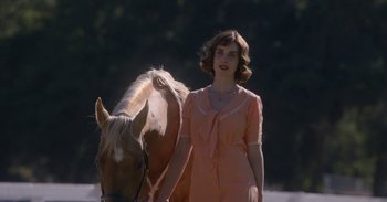 Movie still from “Horse Girl” (2020), directed by Jeff Baena – A woman in a pink dress standing next to a horse; Medium shot, Over the shoulder angle