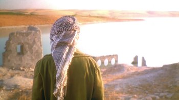 Movie still from “The Bandit” (1996), directed by Yavuz Turgul – A person wearing a headscarf standing in front of a body of water; Medium shot, Over the shoulder angle