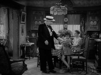 Movie still from “The Bank Dick” (1940), directed by Edward F. Cline – An old photo of a man and a woman at a table with a little girl; Medium shot, High angle