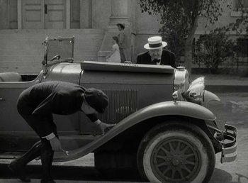 Movie still from “The Bank Dick” (1940), directed by Edward F. Cline – An older man sitting on the hood of an antique car; Wide shot, High angle