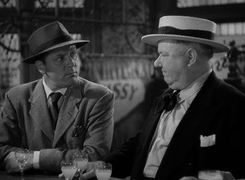Movie still from “The Bank Dick” (1940), directed by Edward F. Cline – A couple of men sitting next to each other at a table; Medium shot, Over the shoulder angle