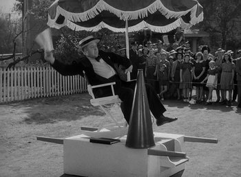 Movie still from “The Bank Dick” (1940), directed by Edward F. Cline – An old photo of a man sitting in a chair on top of an umbrella; Wide shot, High angle