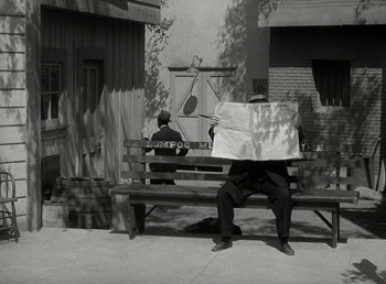 Movie still from “The Bank Dick” (1940), directed by Edward F. Cline – A man sitting on a bench holding a newspaper; Wide shot, High angle