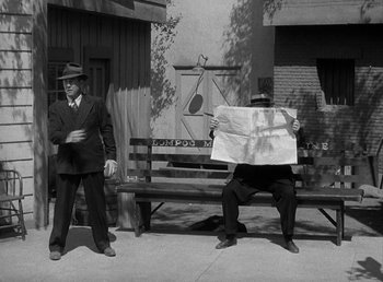 Movie still from “The Bank Dick” (1940), directed by Edward F. Cline – Two men are sitting on a park bench and one of them is reading a newspaper; Wide shot, High angle