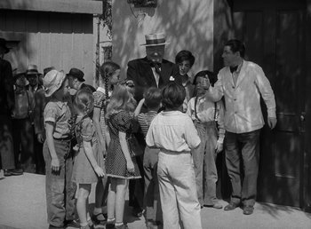 Movie still from “The Bank Dick” (1940), directed by Edward F. Cline – A group of people gathered around a man in front of a building; Wide shot, High angle