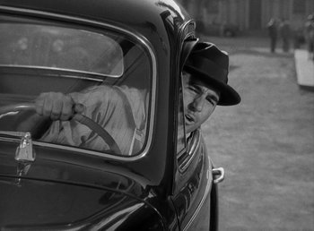 Movie still from “The Bank Dick” (1940), directed by Edward F. Cline – A black and white photo of a man in a hat looking out of a car window; Close Up shot, Over the shoulder angle