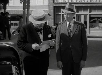 Movie still from “The Bank Dick” (1940), directed by Edward F. Cline – Two men in suits and hats looking at a piece of paper; Medium shot, Over the shoulder angle