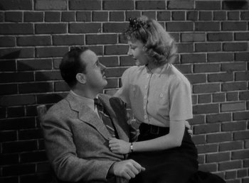 Movie still from “The Bank Dick” (1940), directed by Edward F. Cline – A man and a woman sitting next to a brick wall; Medium shot, High angle