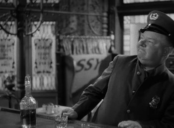 Movie still from “The Bank Dick” (1940), directed by Edward F. Cline – A man sitting at a table with a bottle of alcohol; Medium shot, Low angle