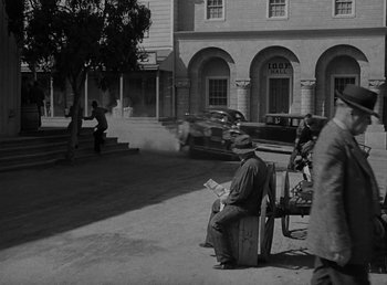 Movie still from “The Bank Dick” (1940), directed by Edward F. Cline – An old photo of a man sitting on a bench in front of a building; Wide shot, High angle