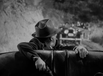 Movie still from “The Bank Dick” (1940), directed by Edward F. Cline – A man with a hat and a gun leaning on a suitcase; Medium shot, High angle