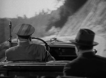 Movie still from “The Bank Dick” (1940), directed by Edward F. Cline – A man driving a car on a road with another man sitting in the passenger seat; Medium shot, High angle