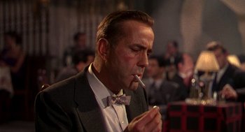 Movie still from “The Barefoot Contessa” (1954), directed by Joseph L. Mankiewicz – A man in a suit and tie smoking a cigarette; Close Up shot, Low angle