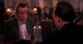 Movie still from “The Barefoot Contessa” (1954), directed by Joseph L. Mankiewicz – A man sitting at a table talking to another man in a suit; Close Up shot, Over the shoulder angle