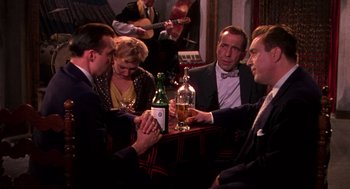Movie still from “The Barefoot Contessa” (1954), directed by Joseph L. Mankiewicz – A group of people sitting at a table with a bottle of alcohol; Medium shot, High angle
