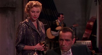Movie still from “The Barefoot Contessa” (1954), directed by Joseph L. Mankiewicz – A man and a woman are sitting next to each other in front of a guitar; Medium shot, Over the shoulder angle