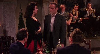 Movie still from “The Barefoot Contessa” (1954), directed by Joseph L. Mankiewicz – A group of people sitting at a table with drinks; Medium shot, Over the shoulder angle
