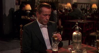 Movie still from “The Barefoot Contessa” (1954), directed by Joseph L. Mankiewicz – A man sitting at a table with a glass of wine; Medium shot, High angle