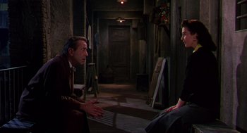 Movie still from “The Barefoot Contessa” (1954), directed by Joseph L. Mankiewicz – A man and a woman sitting in a dark room talking; Medium shot, Over the shoulder angle