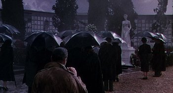 Movie still from “The Barefoot Contessa” (1954), directed by Joseph L. Mankiewicz – A group of people standing under umbrellas in the rain; Wide shot, High angle