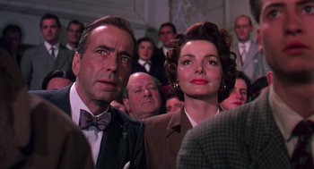 Movie still from “The Barefoot Contessa” (1954), directed by Joseph L. Mankiewicz – A man and a woman are standing in front of a group of people; Close Up shot, Low angle