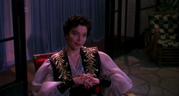 Movie still from “The Barefoot Contessa” (1954), directed by Joseph L. Mankiewicz – A woman sitting on a chair wearing a black and gold outfit; Medium shot, Over the shoulder angle