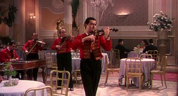Movie still from “The Barefoot Contessa” (1954), directed by Joseph L. Mankiewicz – A man in a red jacket playing a violin in a restaurant; Wide shot, Low angle
