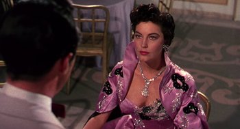 Movie still from “The Barefoot Contessa” (1954), directed by Joseph L. Mankiewicz – A woman in a purple dress sitting in front of a chair; Close Up shot, Over the shoulder angle