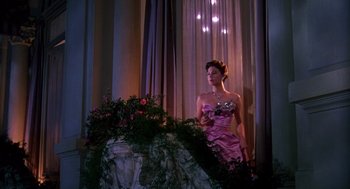 Movie still from “The Barefoot Contessa” (1954), directed by Joseph L. Mankiewicz – A woman in a pink dress standing next to a plant; Wide shot, Low angle