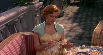 Movie still from “The Barefoot Contessa” (1954), directed by Joseph L. Mankiewicz – A woman in a yellow dress is sewing a dress; Medium shot, High angle