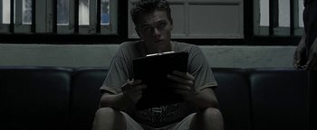 Movie still from “The Beach” (2000), directed by Danny Boyle – A man sitting on a couch looking at a tablet computer; Medium shot, Low angle