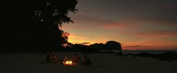 Movie still from “The Beach” (2000), directed by Danny Boyle – A group of people sitting around a fire on the beach; Extreme Wide shot, High angle