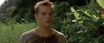 Movie still from “The Beach” (2000), directed by Danny Boyle – A young man with a necklace is standing in the woods; Close Up shot, Low angle